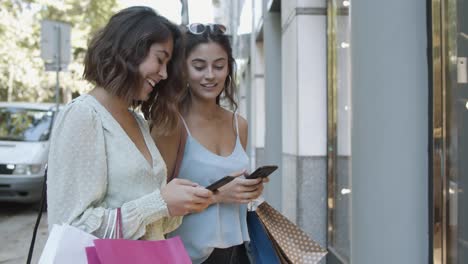 Happy-young-women-standing-on-street-and-using-mobile-phone