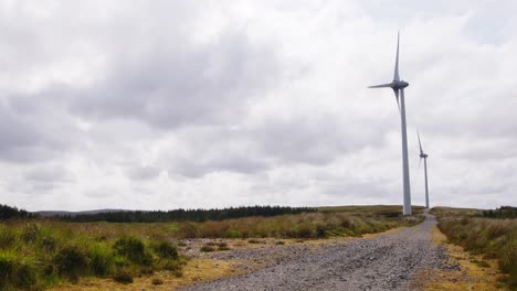 shot of two wind turbines generating electricity by a dirt track road