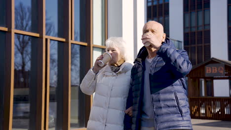 senior couple holding hands and walking down the street on a winter day while they drinking a coffee to go