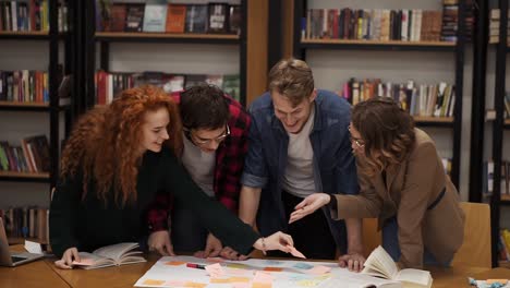 young diverse marketing research team brainstorming working on startup business solution. four people working on a plan. girl pointing on coloured sticker with pen. active discussion. front view