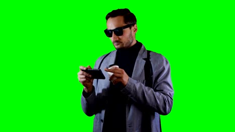 man in suit and black sunglasses type a message on mobile and hold coffee cup. green screen, footage