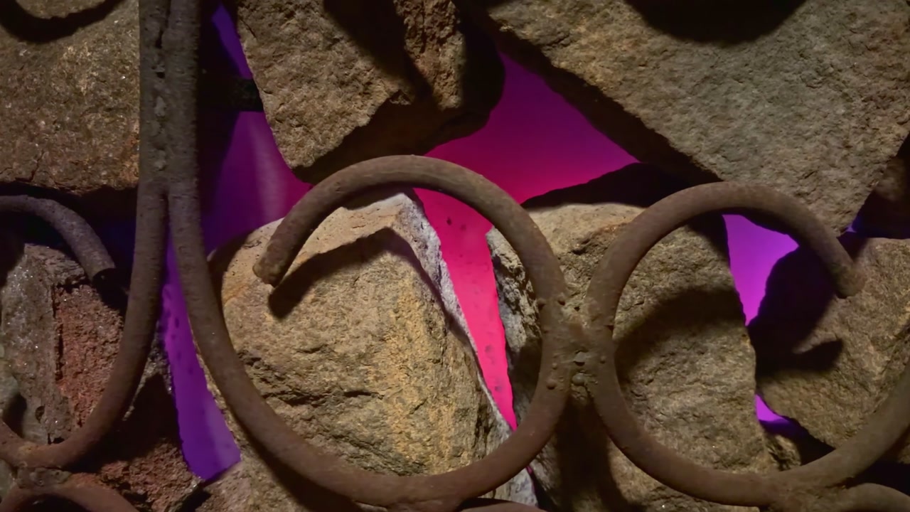 Rusty metal bars intertwining with natural rocks, glowing magenta light in closeup