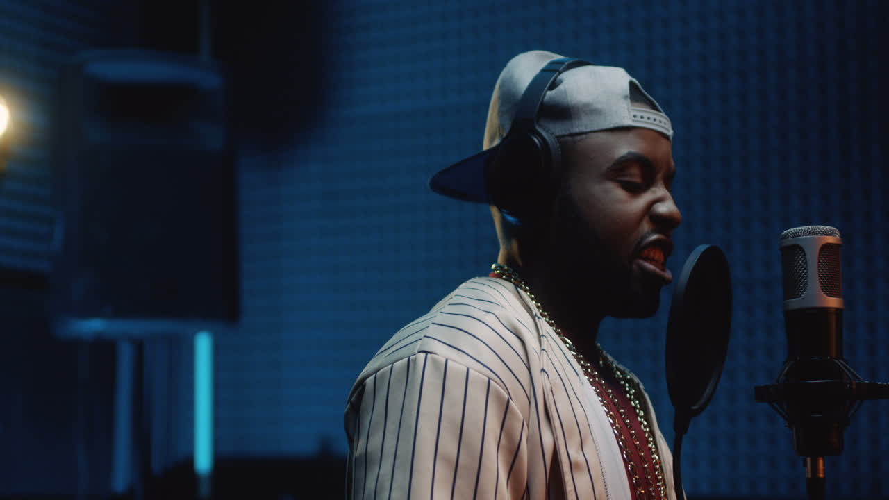 primer plano del joven, guapo y elegante cantante de r'n'b grabando una canción en el estudio mientras canta en el micrófono