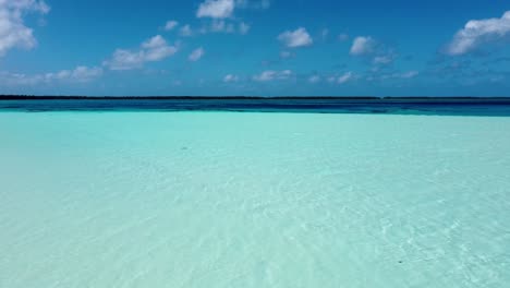 drone view of a young caucasian woman sitting on a white sand tropical pacific beach with shallow water and coral reefs on a sunny day in maupiti, french polynesia.