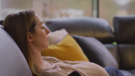 mulher grávida relaxando sentada no sofá em casa assistindo tv