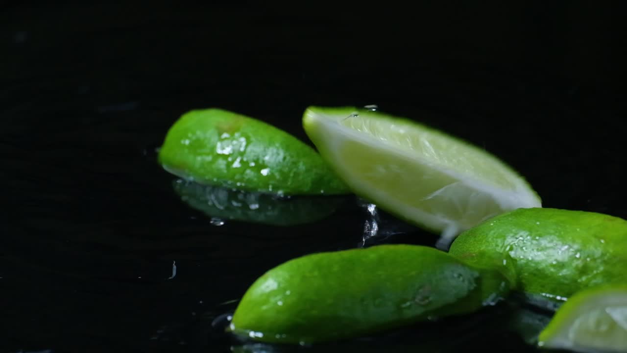 검은 바탕에 고립 된 물 표면에 떨어지는 맛있는 녹색 라임 슬라이스