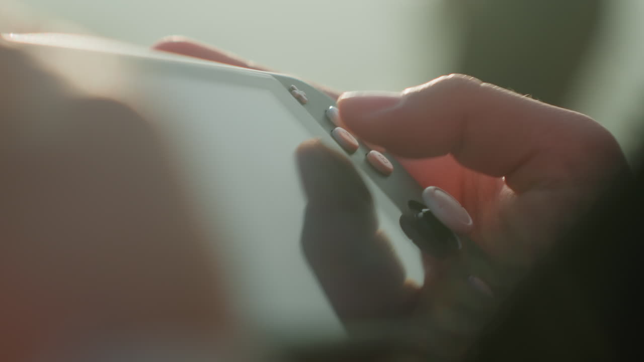 Primo piano di mani su un controller per smartphone. Un giocatore occasionale all'aperto usa il pollice per premere i pulsanti su un accessorio controller compatto; lo schermo che riflette luci soffuse e una scena con un bokeh delicato crea un'atmosfera intima.