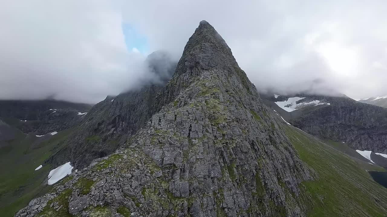 el dron fpv asciende audazmente a una cresta de montaña, rodeado de picos brumosos, revelando un místico mundo alpino desde una emocionante perspectiva aérea
