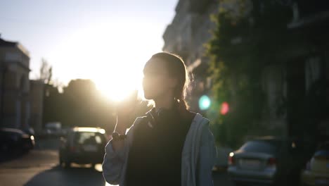 modern, stylish girl standing on the street all in the sunlight and taking ice-cream. son shadows on buildings, sunset dusk