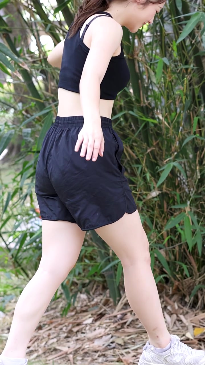 晴れた公園で、黒いスポーツウェアを着たアジア人女性が青い飛び石の上でバランスをとっている。