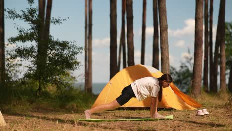 woman practicing yoga in a forest near a campsite