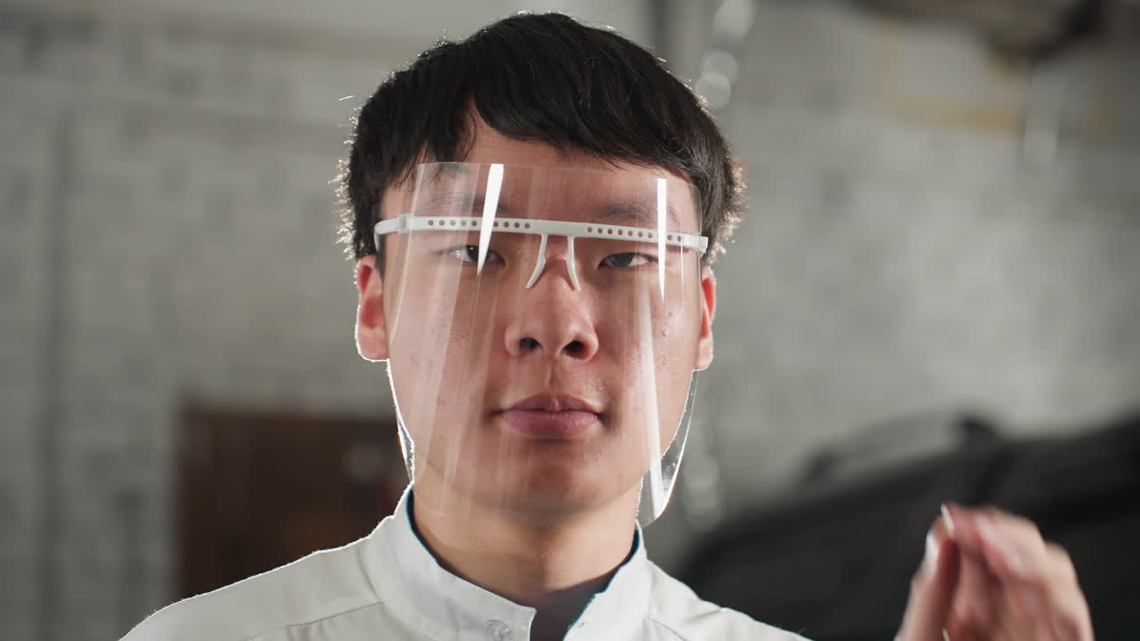 자동차 워크에서 보호 안경을 조정하는 실험실 코트를 입은 엔지니어의 클로즈업, 집중된 표현, 도구와 기계와 함께 산업 배경