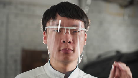 primer plano de un ingeniero en bata de laboratorio ajustando gafas de protección en un taller automotriz, expresión enfocada, antecedentes industriales con herramientas y maquinaria