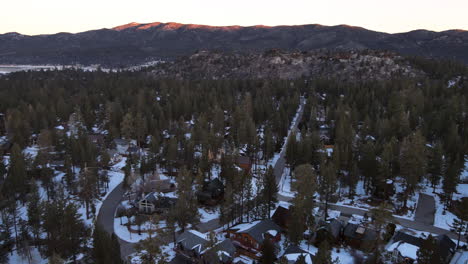 pan aerial drone shot of residential in rural area in winter and snow with pine trees and mountains