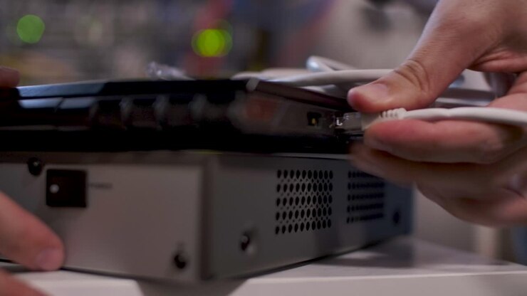En tekniker i serverrummet indsætter et kabel i LAN-porten på en bærbar computer oven på en router.