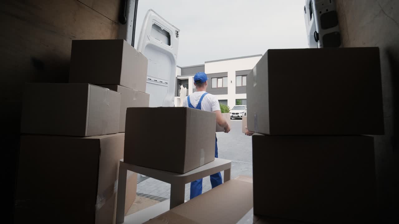 dos jóvenes trabajadores de una empresa de mudanzas descargan cajas y muebles del minibús en la casa del cliente