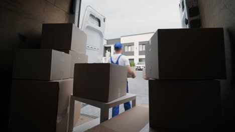 two young workers of removal company unload boxes and furniture from minibus into customer's home