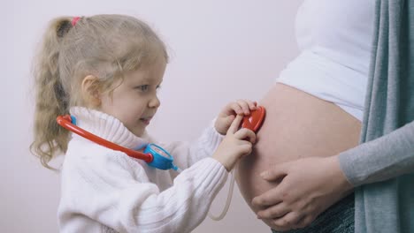 niña con cola de caballo examina a mamá embarazada usando juguetes