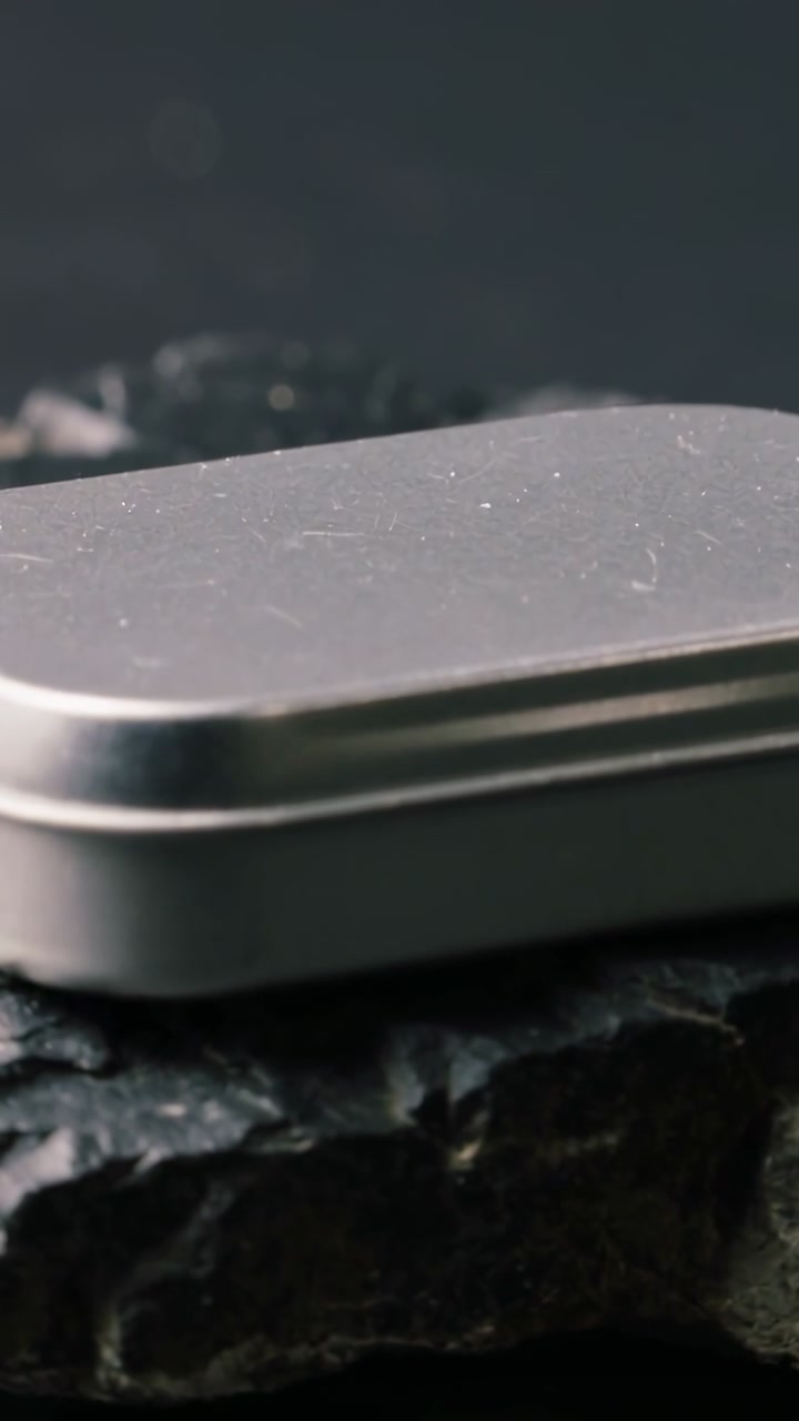 Vertical video: Camera pushing and shifting focus, small silver tin revealing dust, scuffs on slate