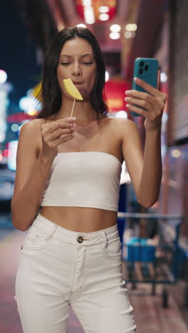 woman taking a selfie with mango stick at night market