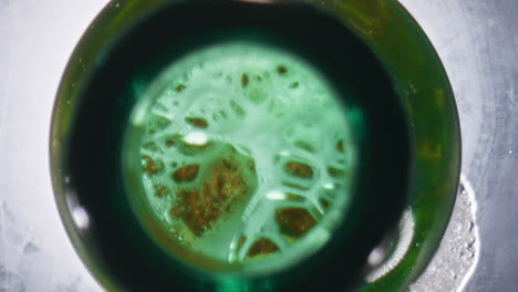 cold ale overflowing bottle closeup. wheat beer making foam green glassy vessel