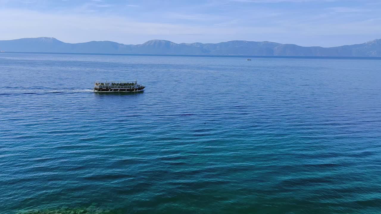 A calm wide view shows a tour boat moving across the blue sea in Croatia with distant mountains creating a peaceful coastal backdrop under clear daylight