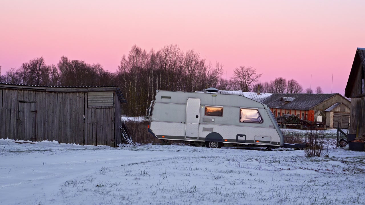 Fritidskøretøj med varmt lys indeni, der står i et vinterlandskab ved skumringstid