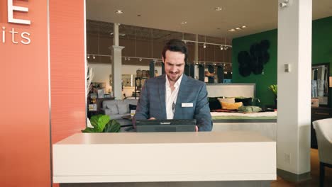 A-Young-Well-Dressed-Professional-Furniture-Store-Sales-Person-Walks-Behind-a-Counter-Surprised-by-Customer