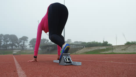 vista trasera de una atleta tomando la posición de salida y corriendo en la pista 4k