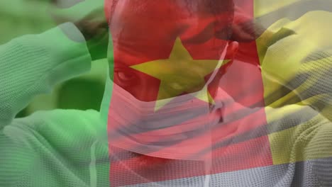 Animation-of-flag-of-cameroon-waving-over-african-american-man-wearing-face-mask-in-city-street