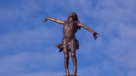 a statue of a young girl with arms wide open embracing the world sits in a wisconsin park