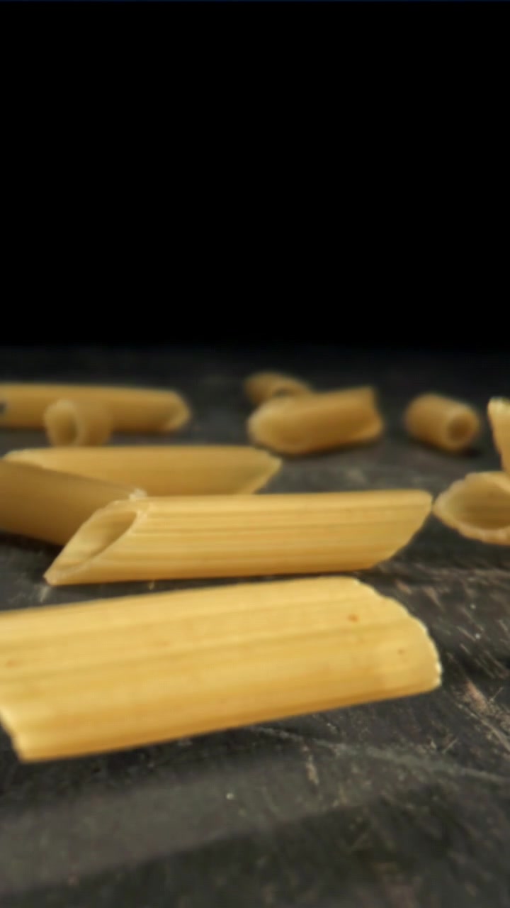 Penne che cadono al rallentatore su una superficie rustica scura