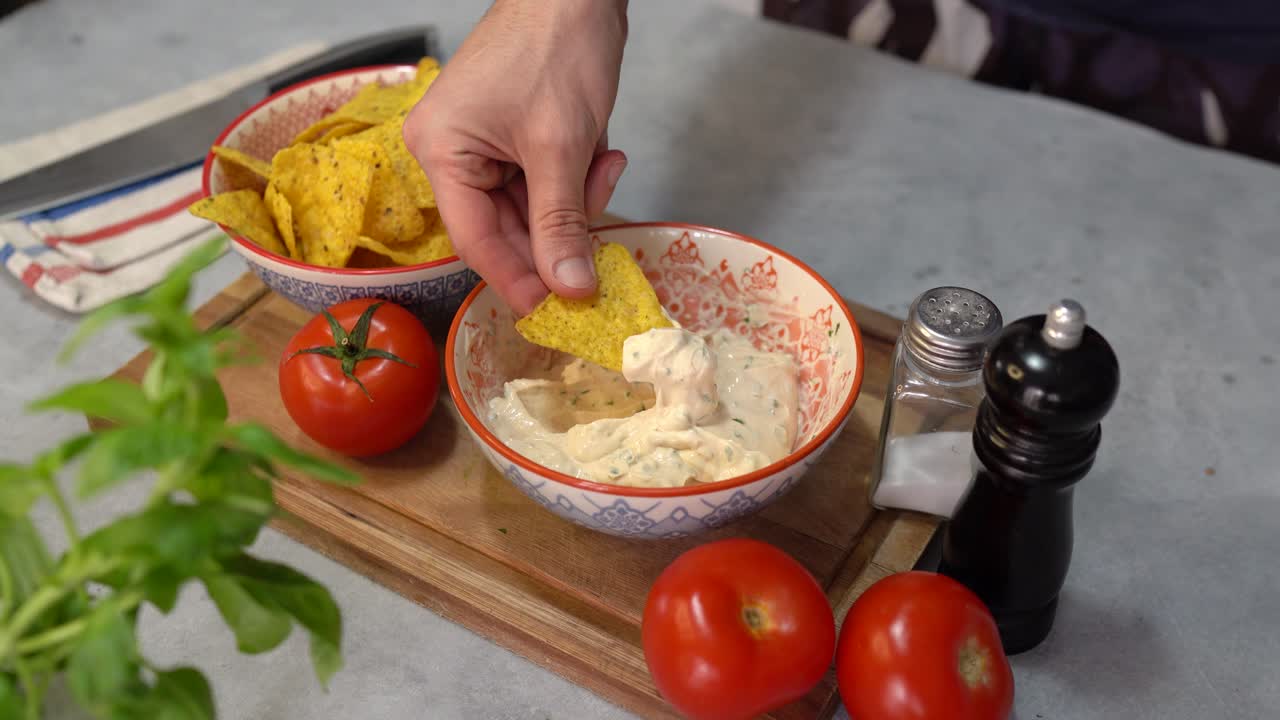 una persona sumerge nachos en pasta de crema de queso