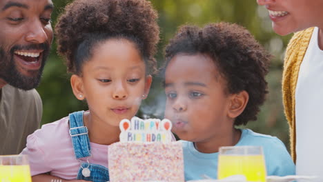 family celebrating child's birthday in garden at home blowing out candles on cake