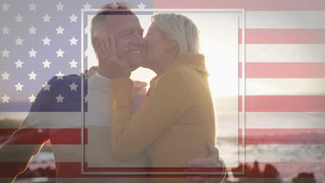 embracing with american flag overlay, elderly couple at beach during sunset