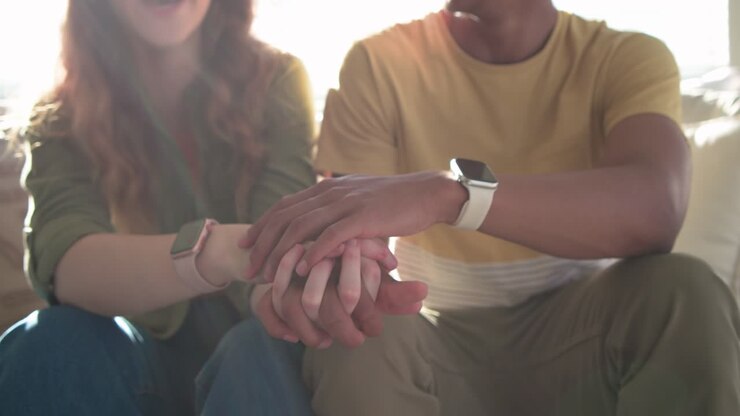 Coppia seduta sul divano con le mani unite, l'uomo che appoggia la mano sulla sua, orologi visibili, che mostra affetto.