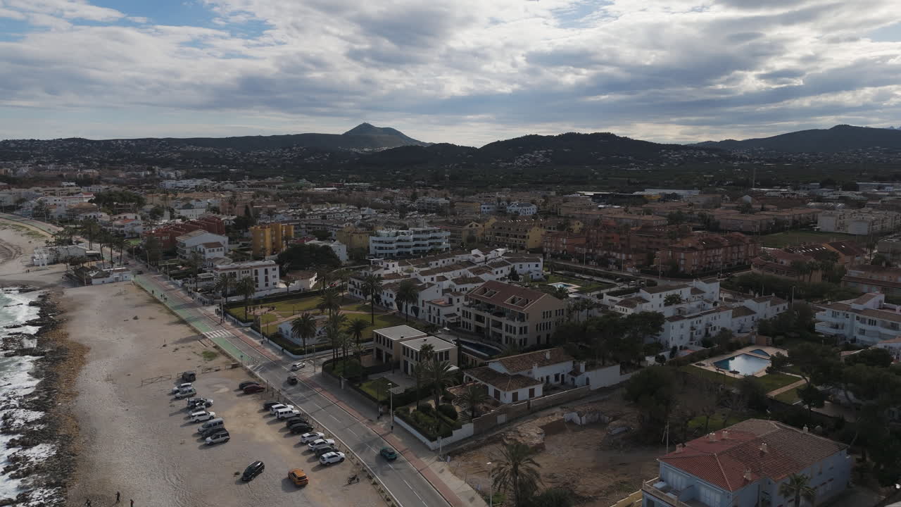 Sweeping cityscape of Xabia reveals rooftops and sea beyond under moody skies