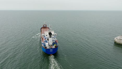 aerial establishing view of large blue cargo ship leaving port of liepaja , karosta bridge, slight overcast day, calm baltic sea, medium drone shot moving forward