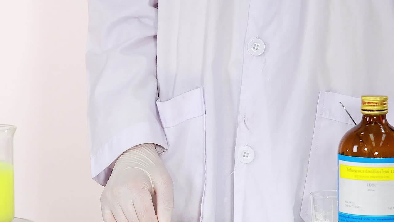 A scientist in a lab coat carefully handles chemical bottles and a dropper in a laboratory setting.