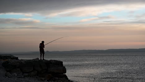 anciano atrapando un pez de un muelle rocoso durante la hermosa puesta de sol de verano