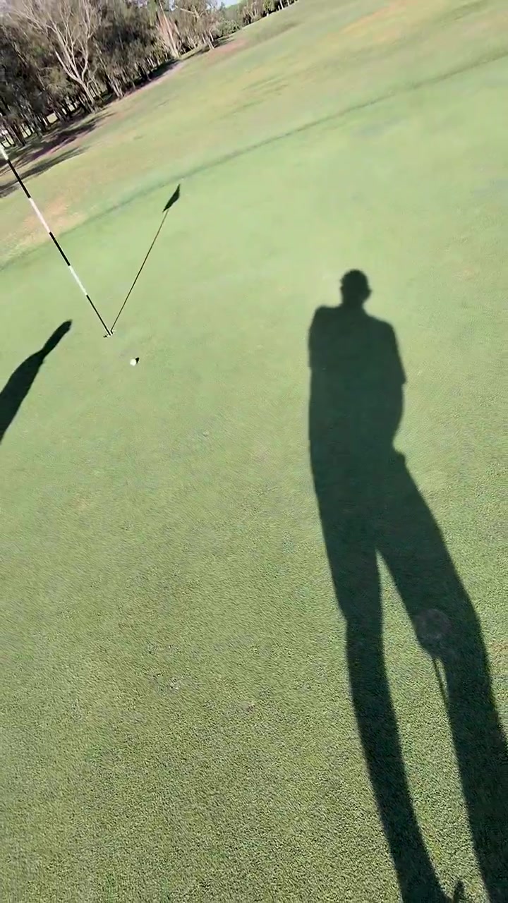 Un golfista in soggettiva cammina attraverso il green soleggiato verso la buca, allineando il putt con un movimento di telecamera a mano.