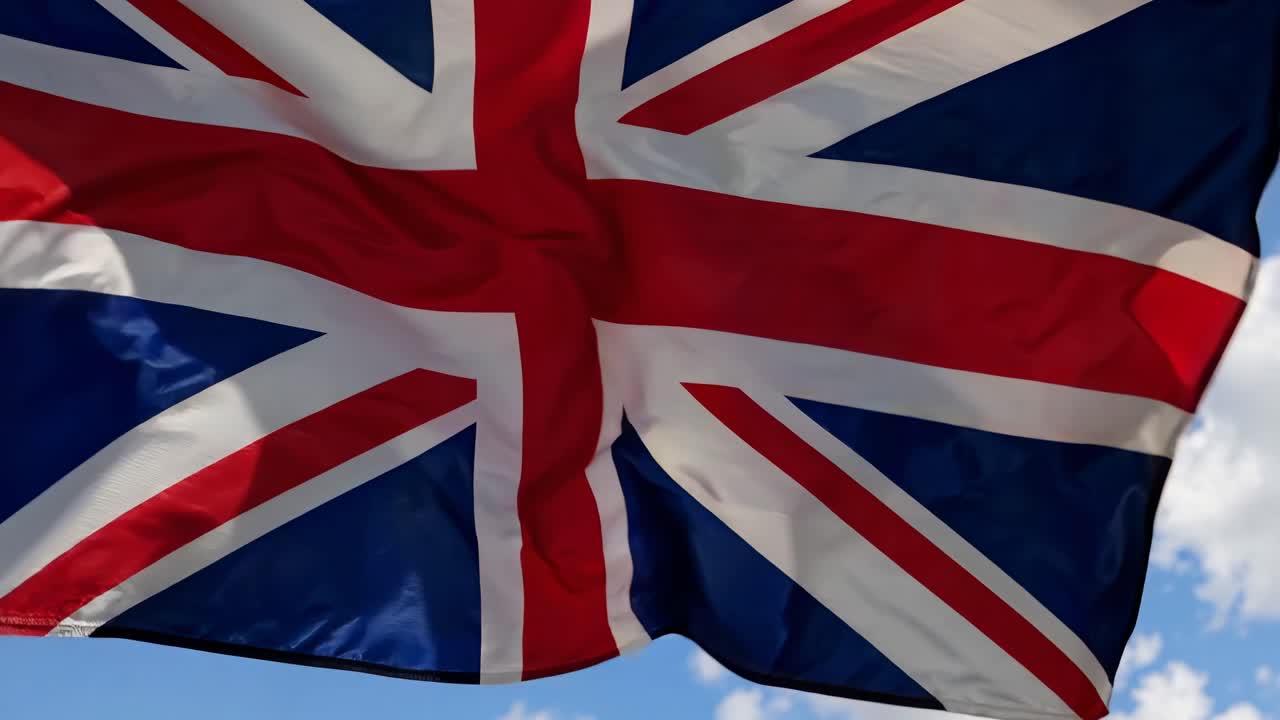 A dynamic low-angle shot of the UK flag waving against a clear blue sky, capturing movement