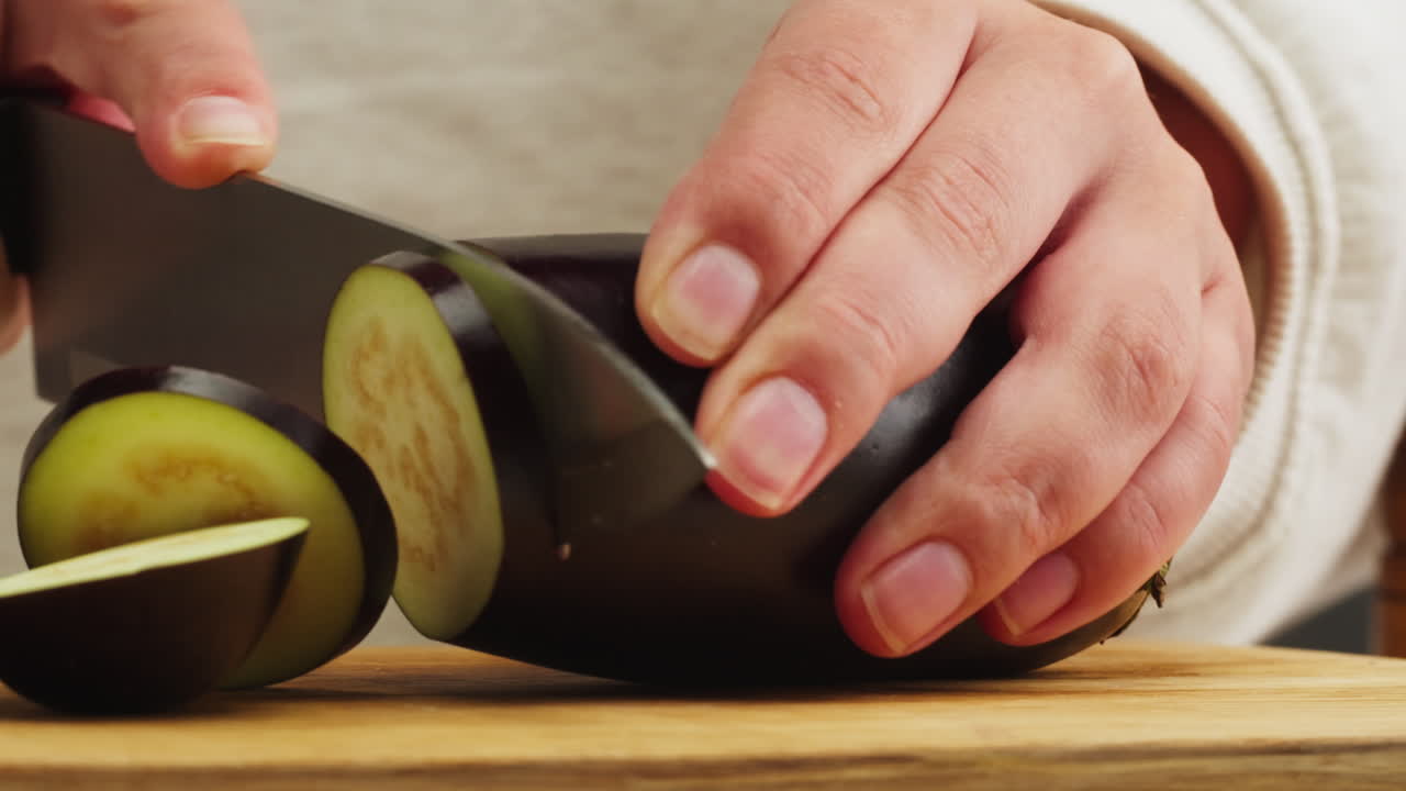 Primo piano di mani che affettano una melanzana fresca su un tagliere di legno