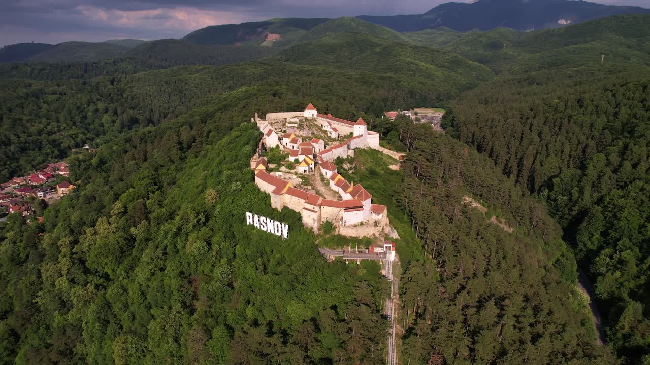 Cittadella di Rasnov in mezzo a foreste lussureggianti sotto un cielo sereno, di giorno, vista aerea.