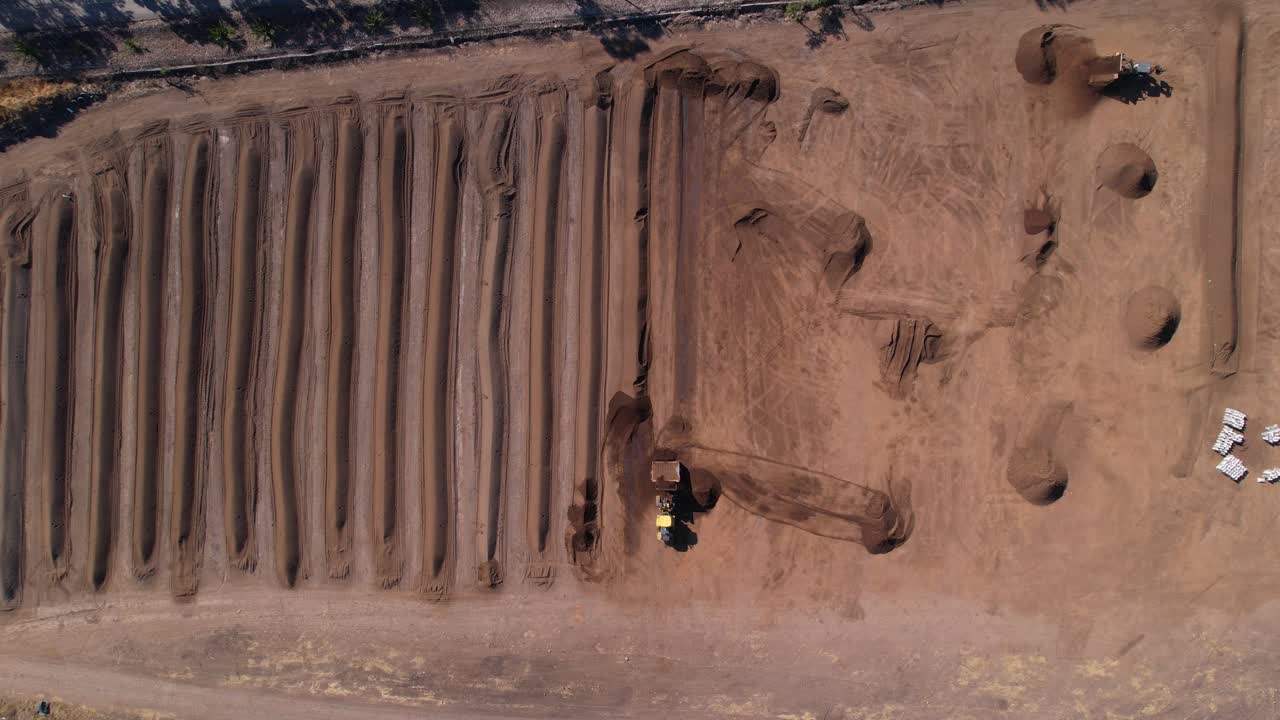 Langsom droneoptagelse, der zoomer ind på kompost, som bearbejdes af en gul traktor på en farm.