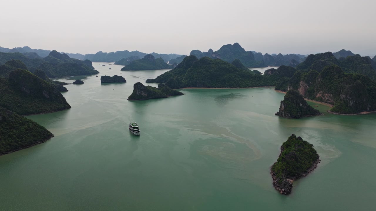 Cảnh trên không của tàu du lịch di chuyển qua các eo biển nước lặng giữa các đảo đá vôi karst nhiệt đới.