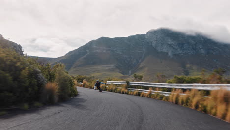 young man riding longboard skating fast enjoying competitive race cruising downhill on beautiful countryside road using skateboard wearing protective helmet