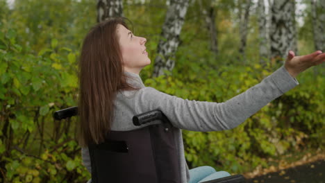 mujer sonriente en silla de ruedas atrapa gotas de lluvia con la palma abierta