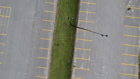 Birds-eye-view-drone-shot-of-a-silver-car-parking-in-an-empty-parking-lot-outside-during-a-sunny-day