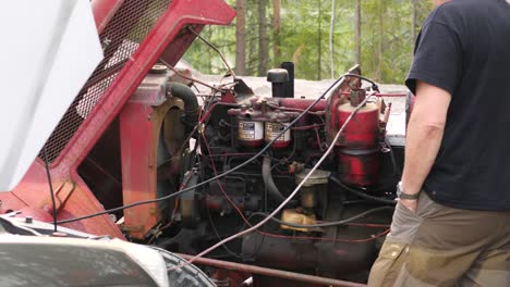 Static-shot-of-a-man-checking-if-a-old-tractor-motor-is-running-as-it-should,-getting-ready-to-repair-it,-on-a-sunny-day,-in-Ostrobothnia,-Finland